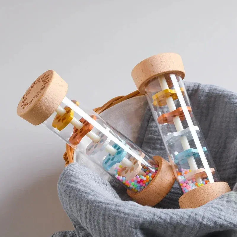 Wooden toy with colorful beads inside a clear tube, held by a gray fabric.
