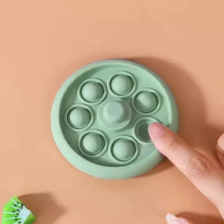 Green pop-it fidget toy with a hand pressing one of the bubbles on a peach background